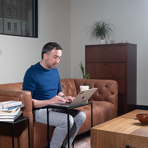 Student types on laptop in on a couch in a coffee shop