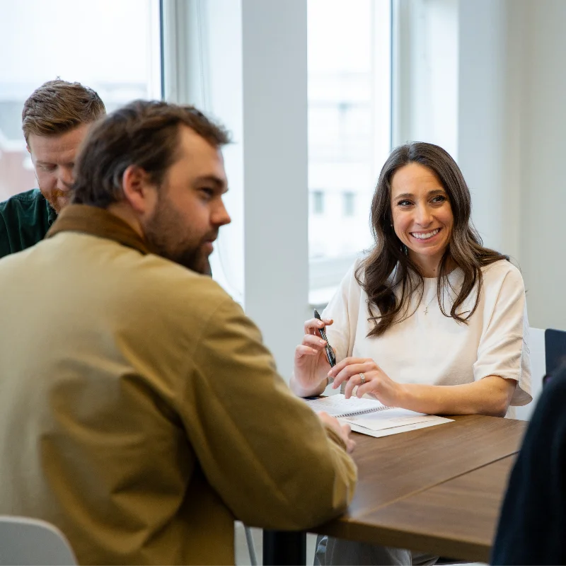 Smiling woman with a pen and notebook, collaborating with male colleagues at a business meeting.