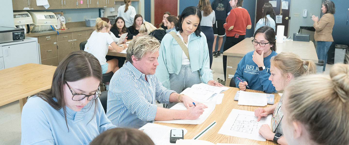 A group of students working with 2 professors at a table examining blue prints