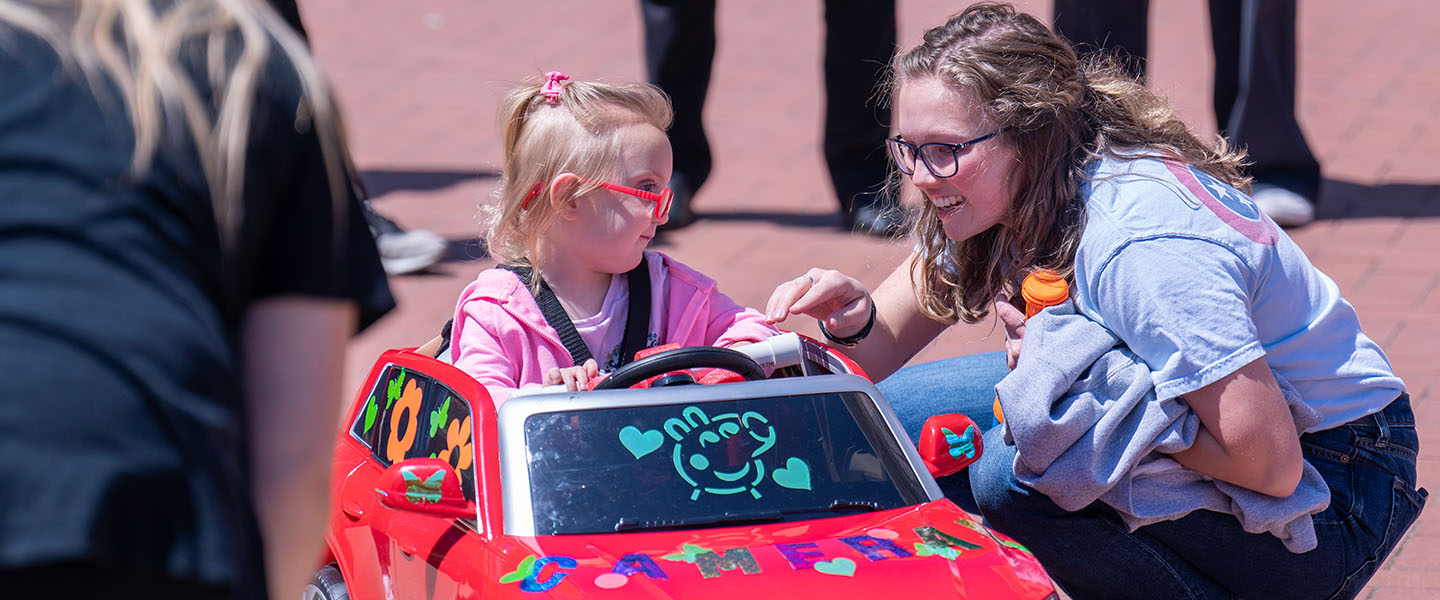 An OT student working with a child in a toy car during Go Baby Go