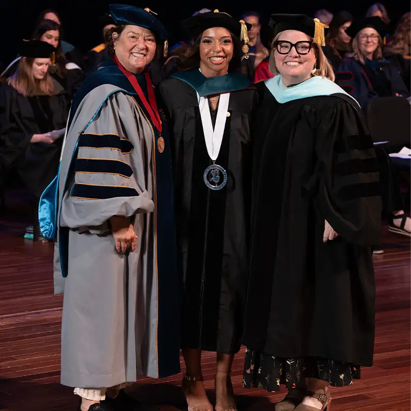 Doctoral graduate posing with two faculty members in academic regalia at Belmont University's graduation event