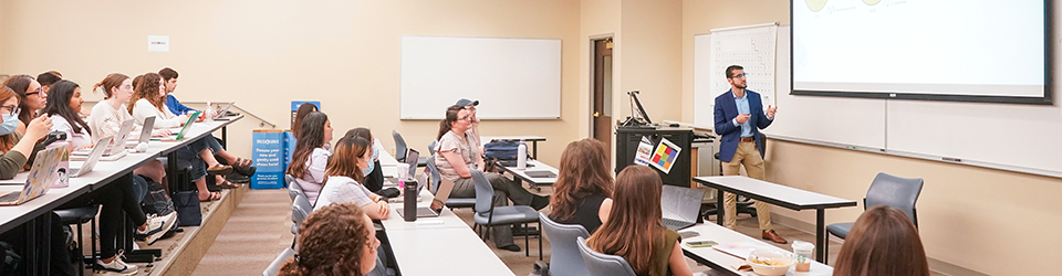 Students leaning in a classroom as teacher speaks