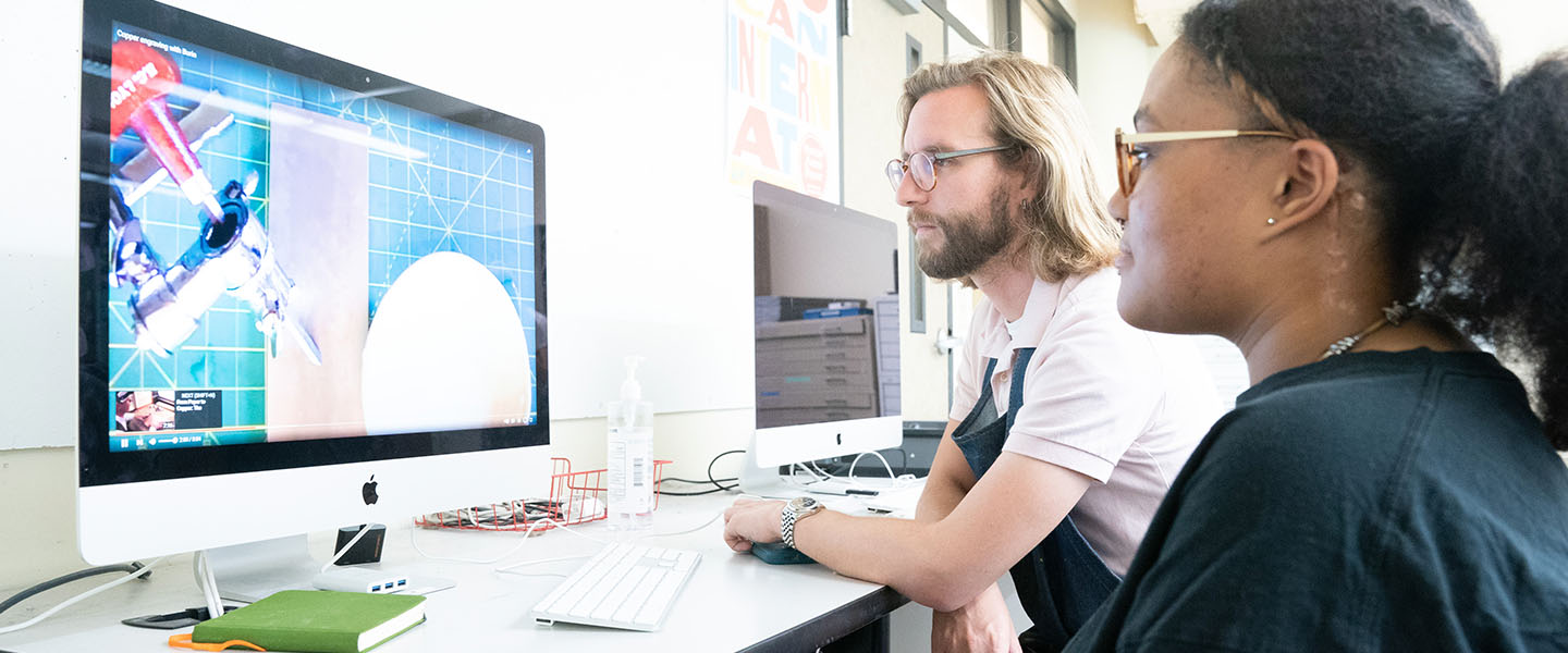 A student and a professor working on a computer in a design class