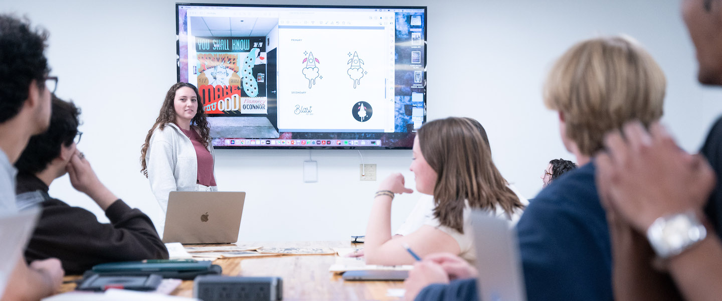 Graphic design students sit around a table for a presentation