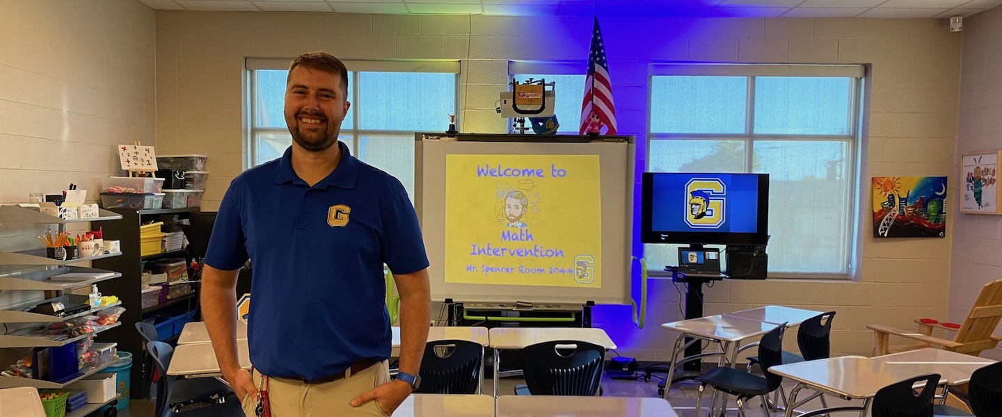 Graham Spencer stands in his classroom in front of a white board that reads Math Intervention