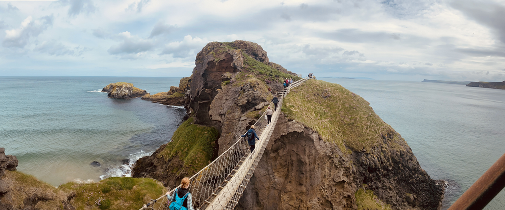 People walking across rope bridge in Ireland cliffside