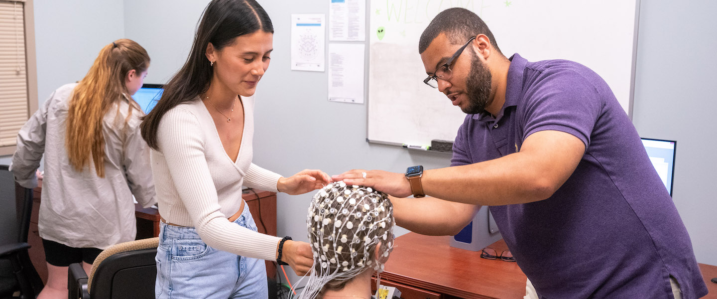 a student and faculty member place EEG cap on a research participant's head