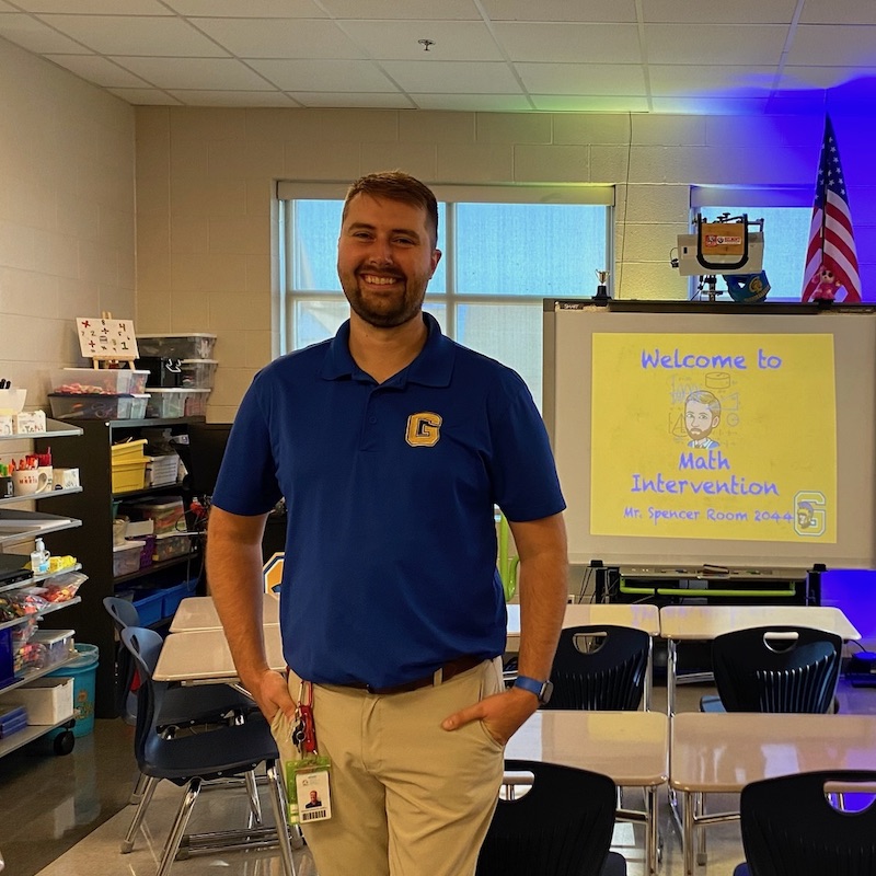 Graham Spencer stands in his classroom in front of a white board that reads Math Intervention