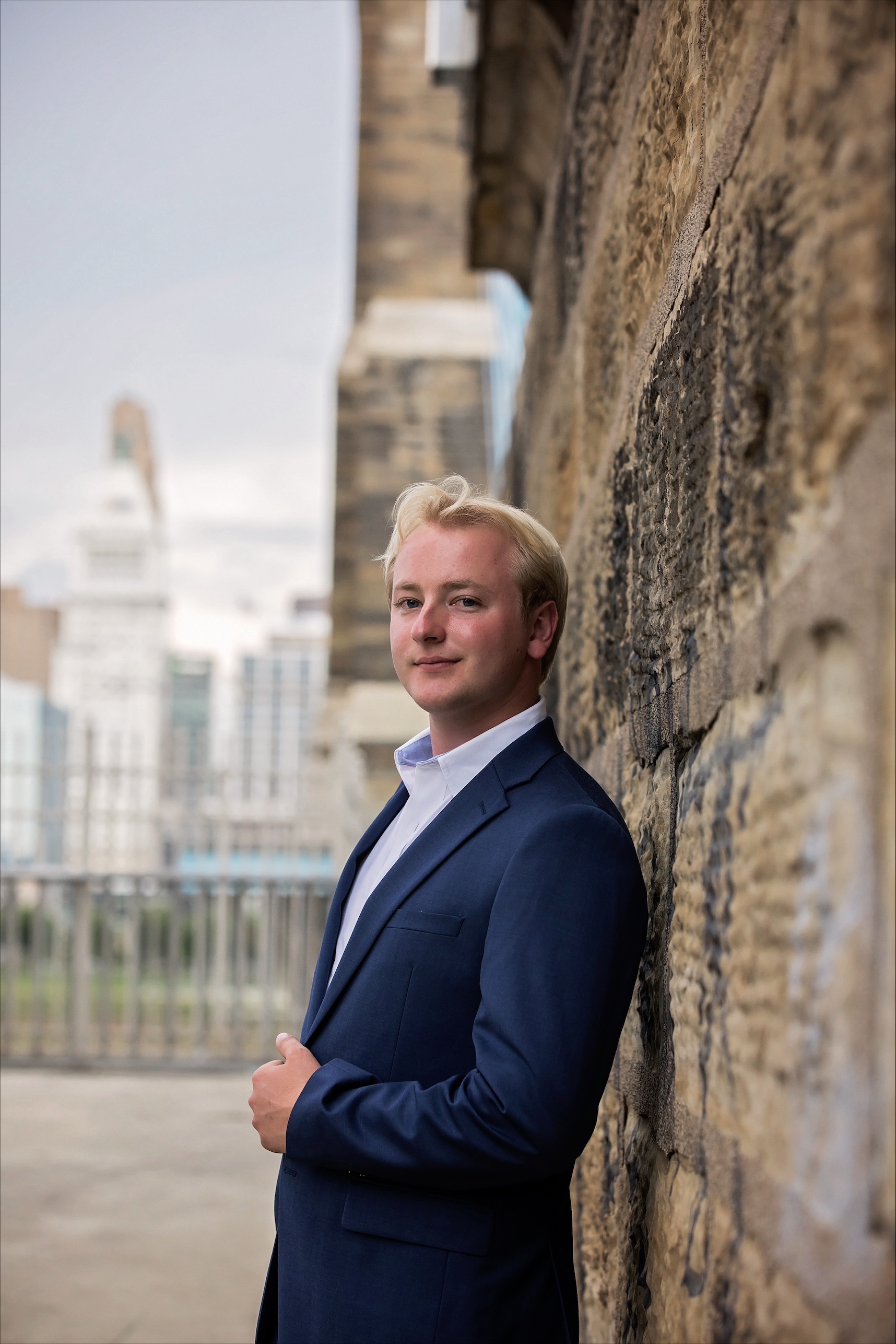 Liam Sweeney headshot in a suit leaning against a wall