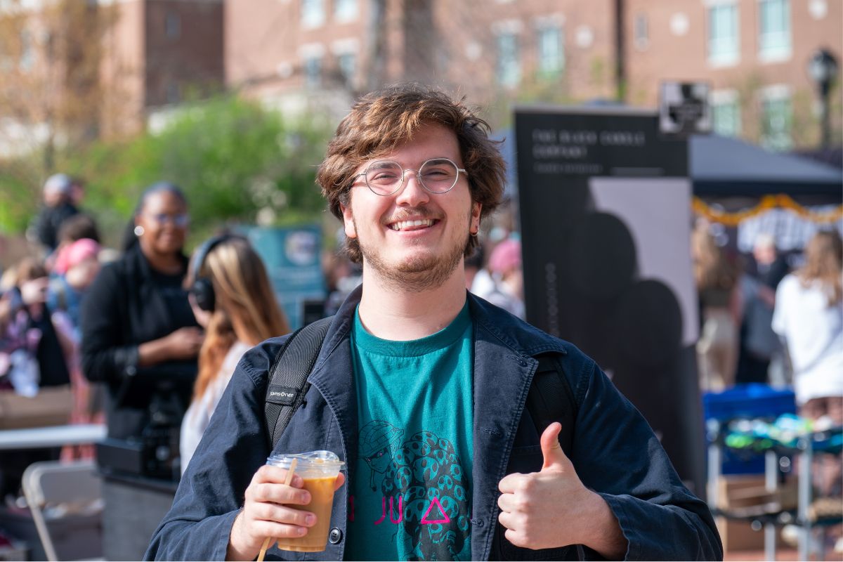 Male student smiling and holding a coffee