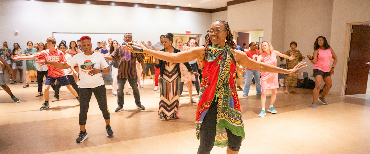 Woman in multicolored African dress leads a group of people dancinge 