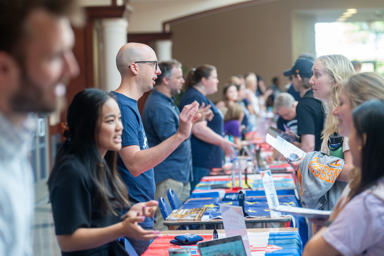 Row of students and faculty talking at organization fair inside campus building