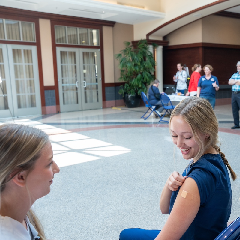 Student smiling with a bandage on her arm after receiving a flu shot