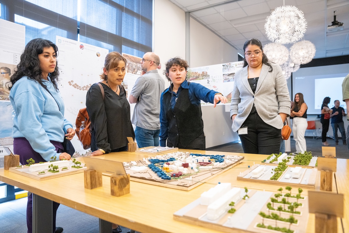 Student explains a detailed site model to guests gathered around a presentation table at the exhibit.