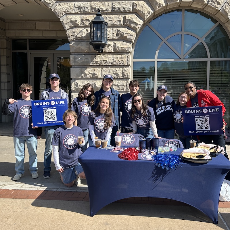 A group of Bruins for Life volunteers outside at a table holding up signs with QR codes.