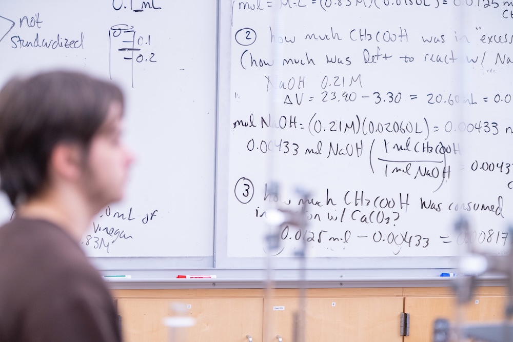 A student sits in front of a whiteboard 