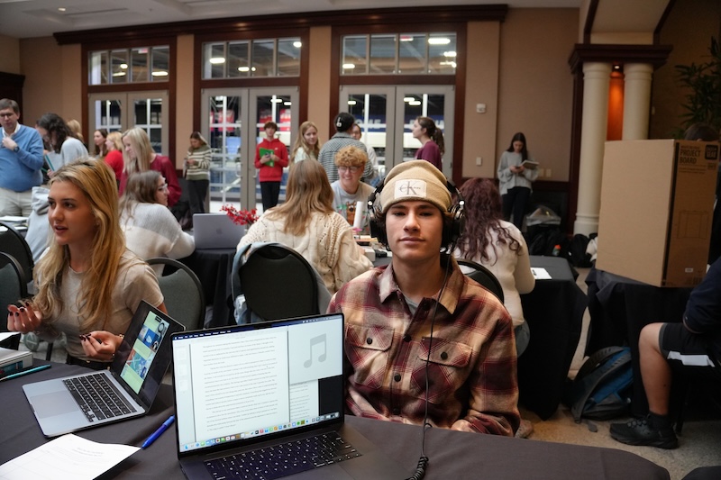 Student poses with headphones next to original song composed for Journey Showcase