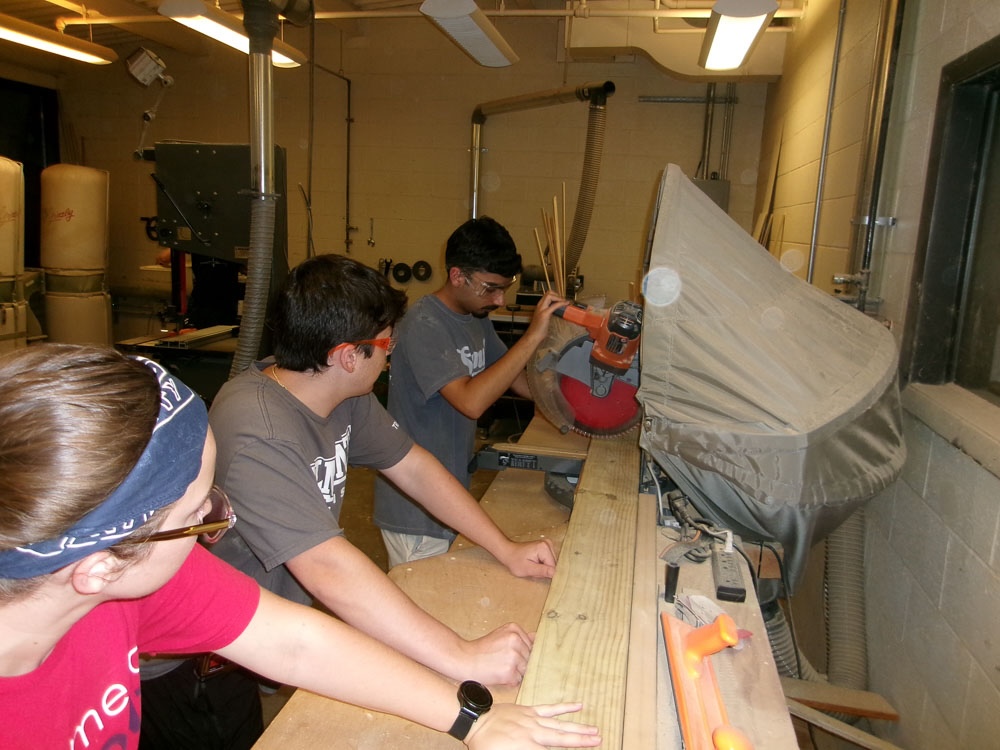 three students using wood saw