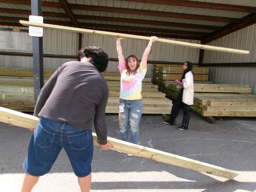 a student smiling and holding a wood beam overhead