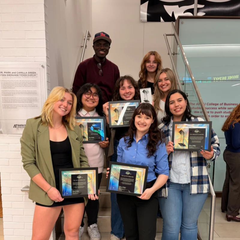 Design students staggered on steps while holding awards.