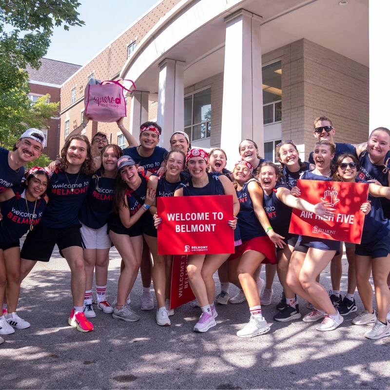 Greg and Susan Jones stand with group of Belmont students and staff in "Welcome to Belmont" shirts on campus during orientation.