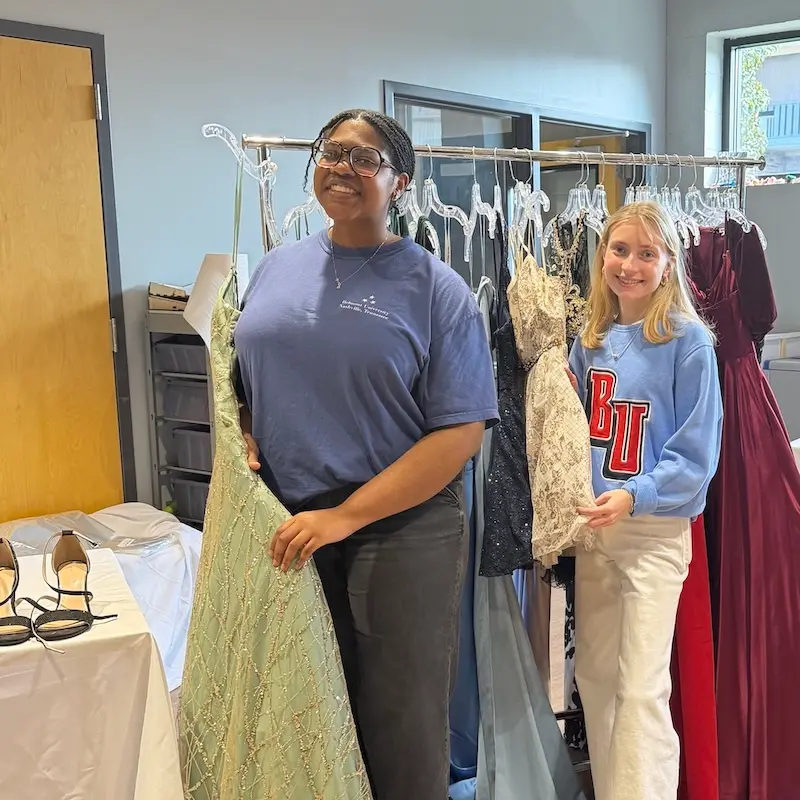 Students standing in front of formal wear clothing rack