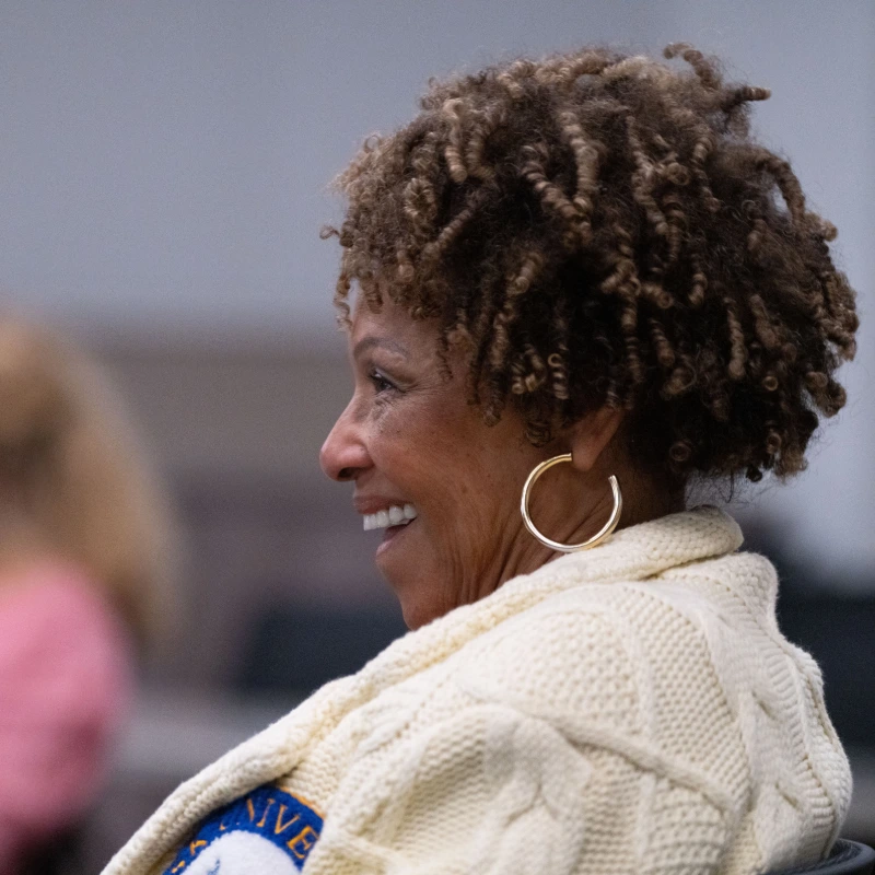 Professional woman with glasses and curly hair presenting or leading a discussion in a modern classroom.