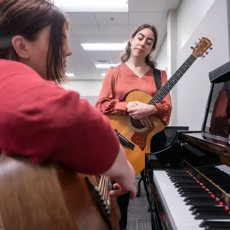 a woman holding a guitar meeting with another woman playing piano