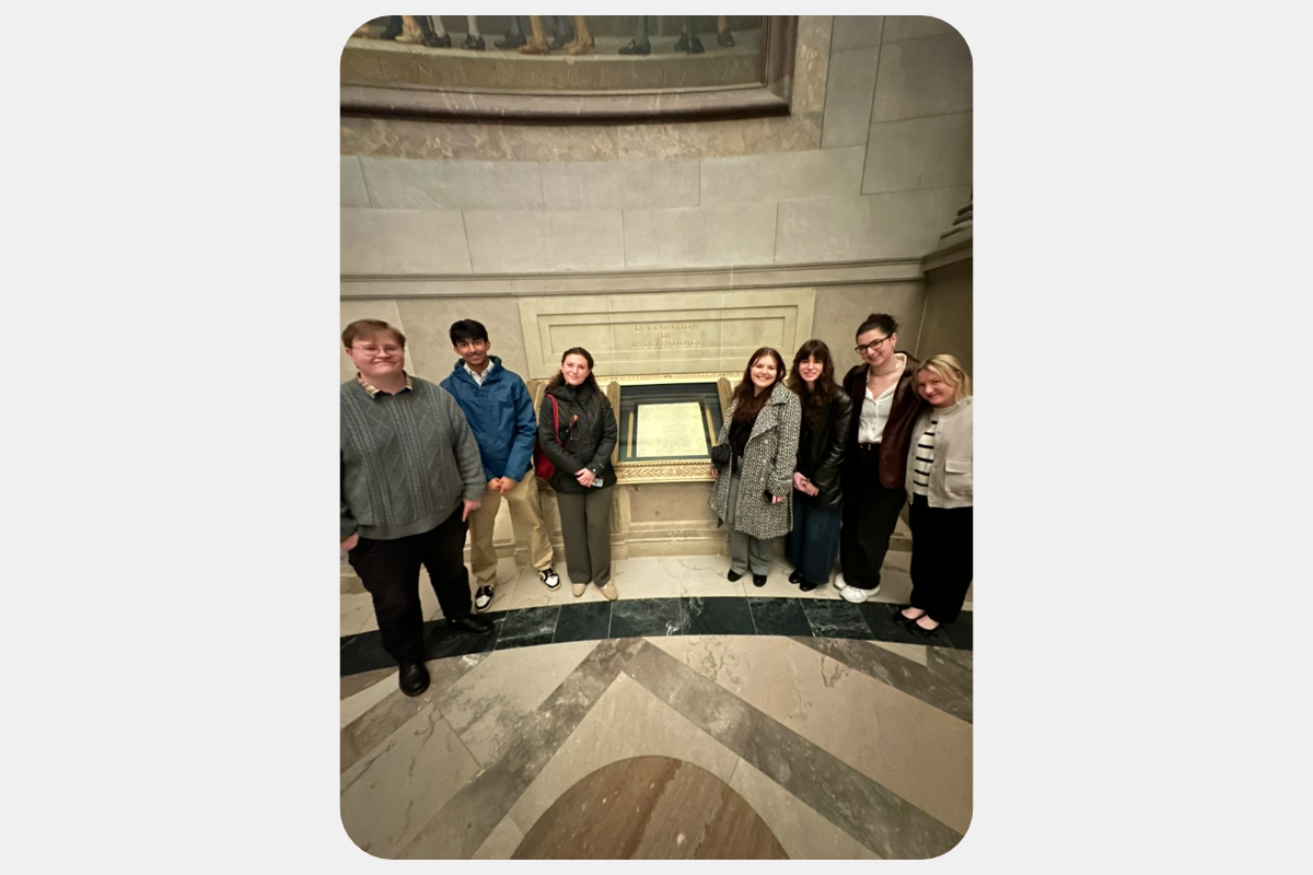 Seven people view a framed historical document exhibit