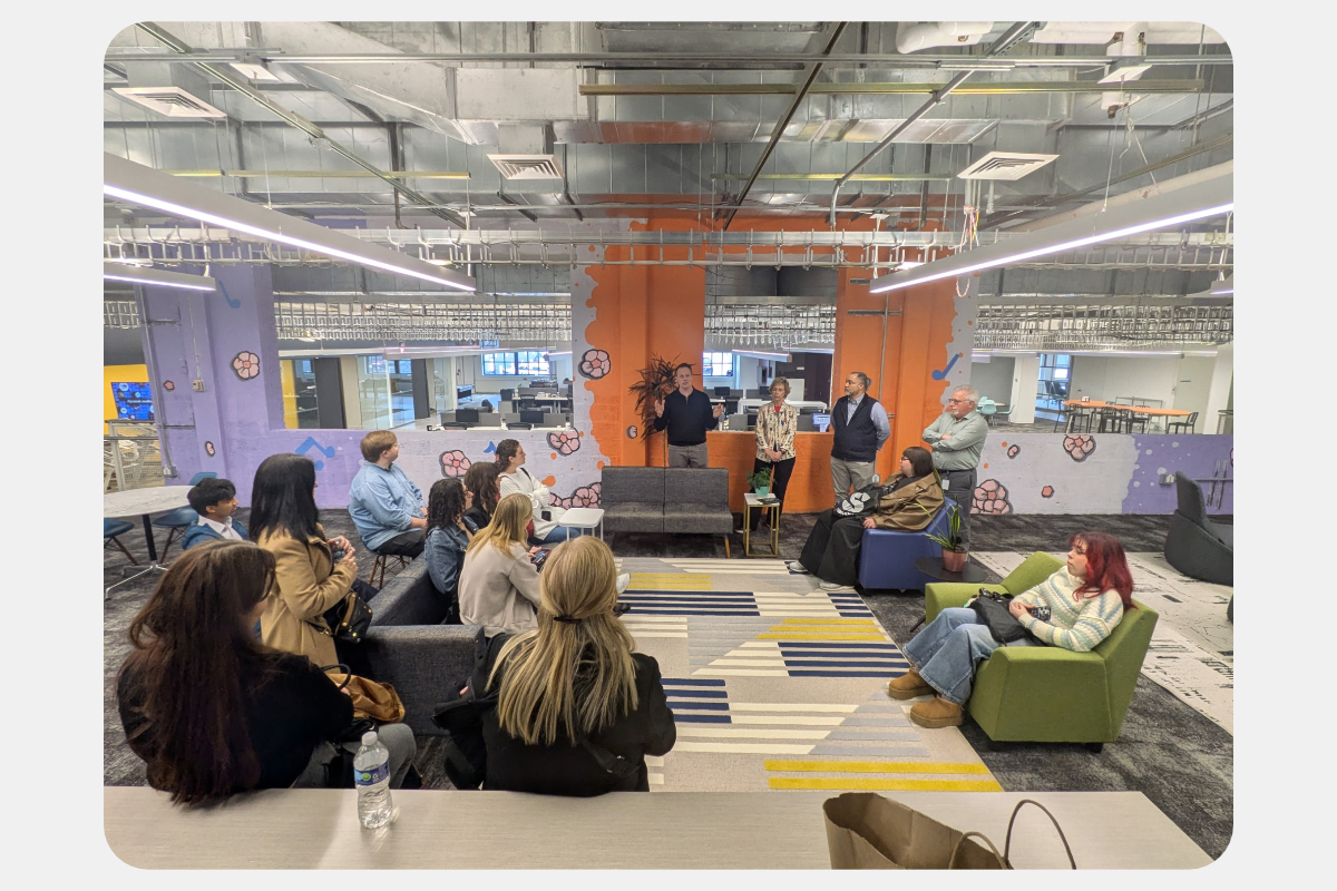 Employees attend an informal meeting or presentation in a colorful, modern open-plan office.