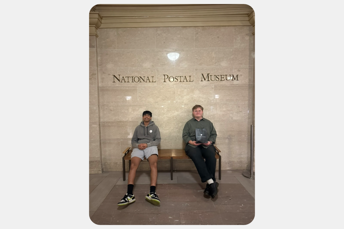 Two visitors sit on a bench in front of the 'National Postal Museum' sign, ready to explore exhibits.