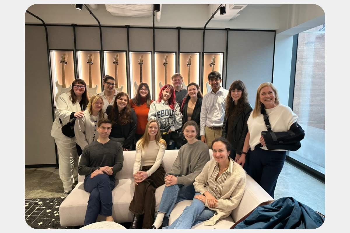 Diverse group of students and professionals smiling in an office, with electric guitars displayed on the wall.