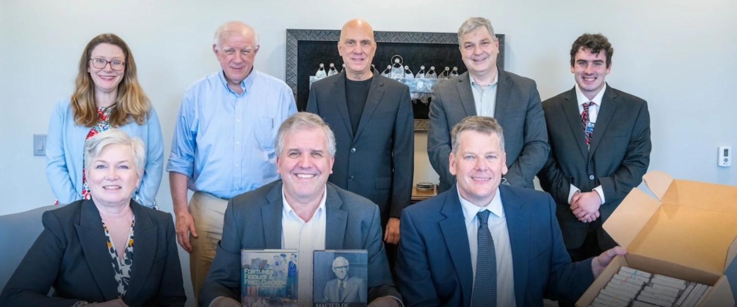 Professional men and women seated at a boardroom table with books and cassette tapes
