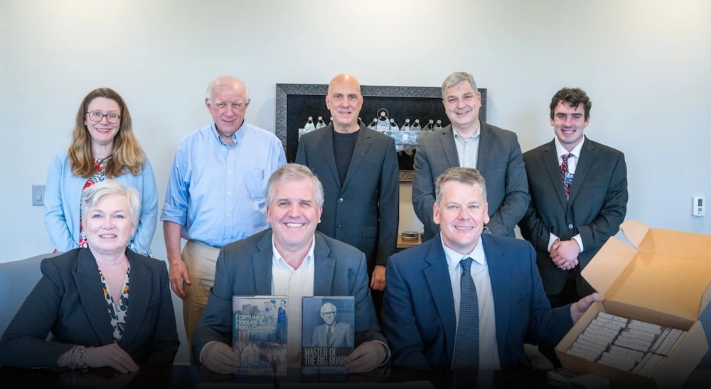 Professional men and women seated at a boardroom table with books and cassette tapes