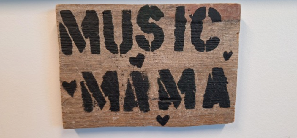 Rustic wooden sign with "MUSIC MAMA" stenciled in black, featuring small heart accents.