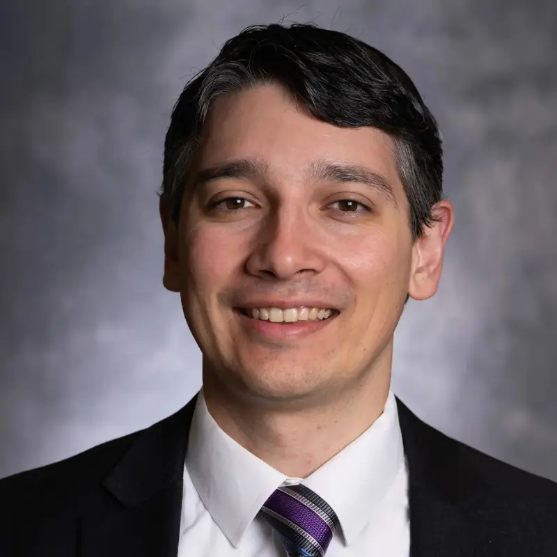 Smiling man in a suit and striped tie against a gray studio background.