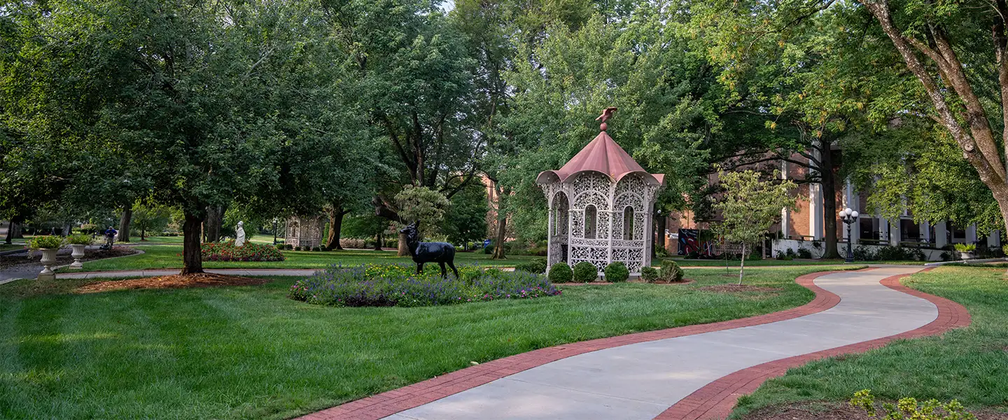 A winding pathway leads to a gazebo surrounded by vibrant greenery and flower beds on the Belmont University campus.