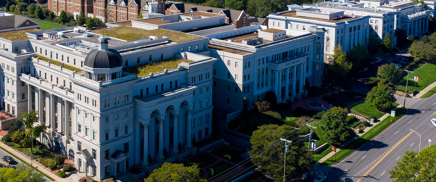 Aerial view of Belmont University's campus, showcasing the Janet Ayers Academic Center and surrounding buildings, with a backdrop of lush greenery and distant hills.