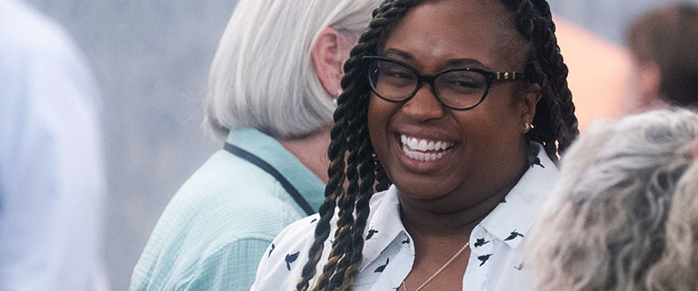 A woman smiling and engaging in conversation with others during a social event or gathering.