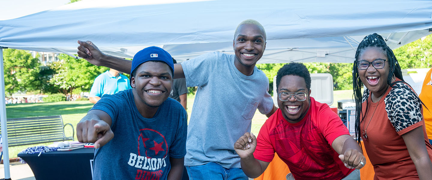 A group of students stand together smiling and pointing enthusiastically at the camera.