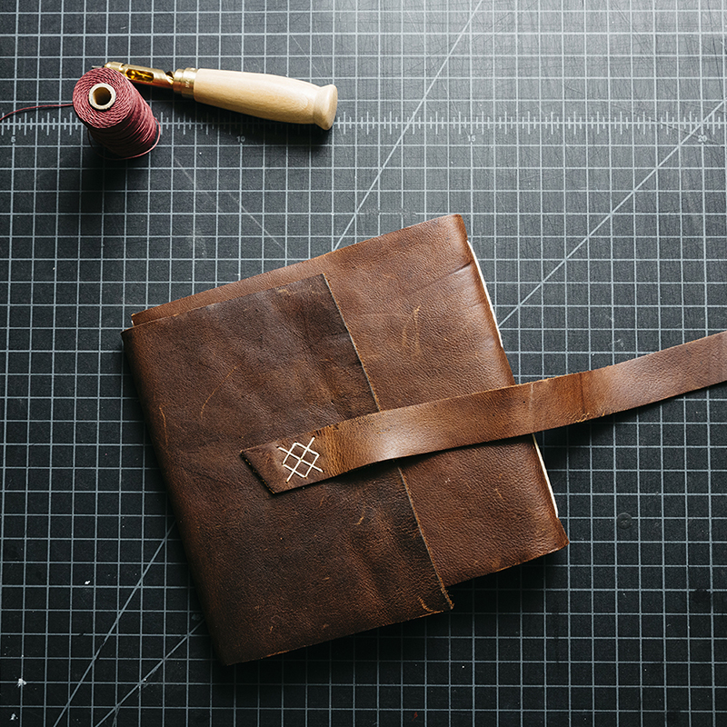 image of a handmade leather journal on a table with book making tools and thread