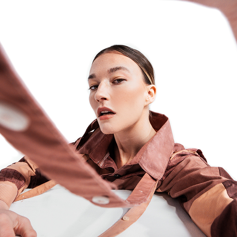 A selfie of a female teen with brown hair with a fisheye lens. She is wearing a brown leather trench coat.