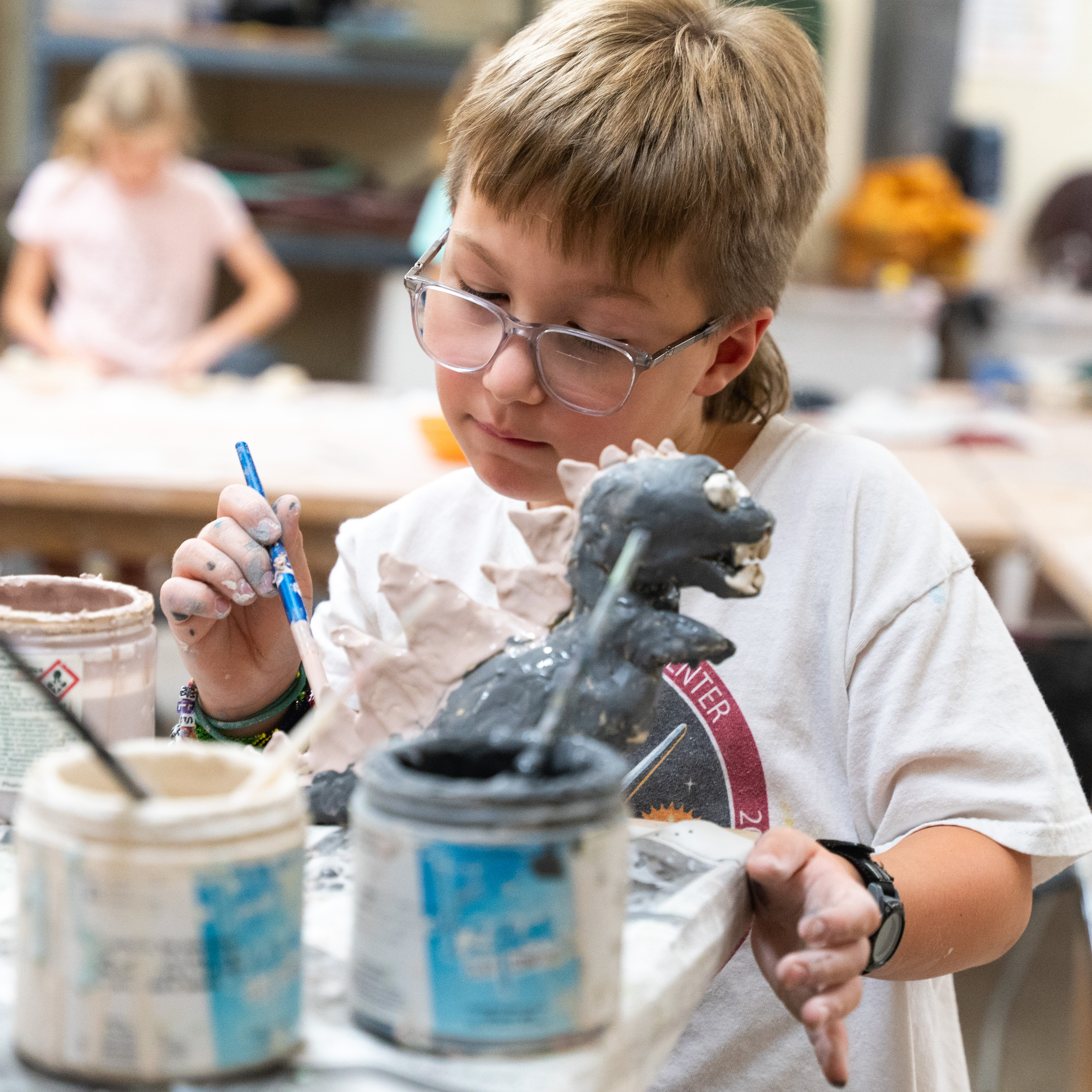 Kid painting a clay sculpture of a dinosaur.
